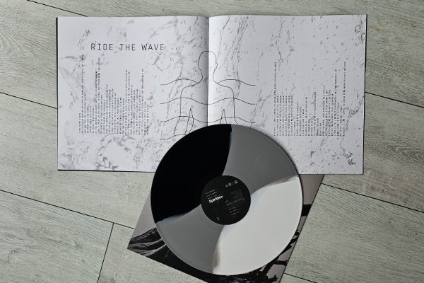 Zdjęcie wnętrza okładki płyty zespołu Spiritbox pt. "Tsunami Sea" otwartej na tekście piosenki "Ride The Wave". Tło to czarno-białe zdjęcie morskich fal z przewagą koloru białego. Tekst piosenki podzielono na dwie części. Jedna znajduje się na stronie lewej, droga na prawej. Po środku, na zgięciu stron znajduje się piktogram przedstawiający człowieka wśród fal. Na zdjęciu znajduje się także płyta winylowa w kolorze czarnym, szarym i białym.
