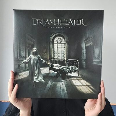 Młoda kobieta trzyma w rękach okładkę płyty winylowej Dream Theater Parasomnia. Nie widać jej twarzy. Zasłania ją płyta winylowa.